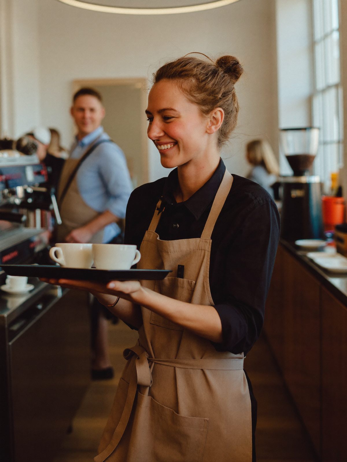 Smiling waitress carrying a tray of coffees through a busy cafe